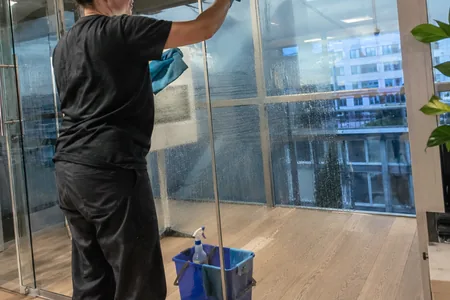 The cleaner washes the floor-to-ceiling glass wall with a view of the city with a cloth, the detergent is sprayed on the cloth, not on the glass, so that the drops don't get on the frames.