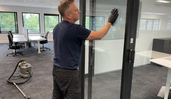 The cleaner wipes the glass partition of the open office with a cloth, the round traces of the installers' suction lifts are removed from the glass as part of the post-construction cleaning price.