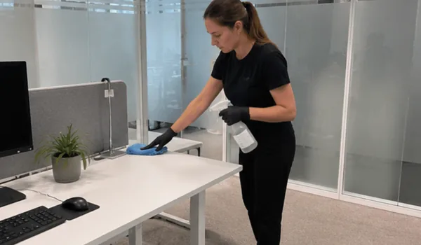 The cleaner wipes the desktop in the glass-walled office with a sprayer and cloth, the circle goes clockwise in each room so that no handle is missed.