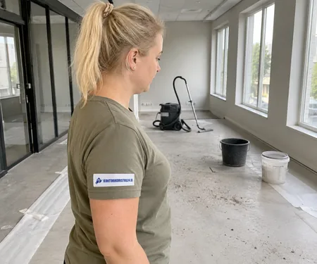 On the sleeve of the cleaner with the logo mark on the post-construction site in front of the vacuum cleaner and buckets, the site supervisor checks each room before handing over.