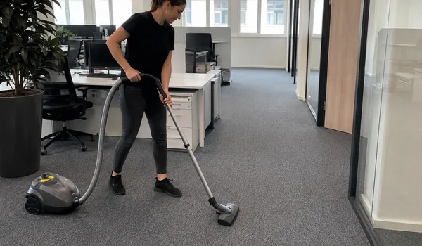 The cleaner vacuums the dust from the open office carpeting between the desks, the vacuum cleaner goes over the entire carpet from wall to wall, not just over the walkways, on each visit.