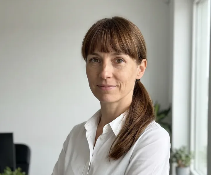 Site manager Kadri Põldsaar with brown hair in bangs, a ponytail falling on her shoulder and a white shirt in front of the window, the site supervisor checks the expiration date of the disinfectant kept at the site during the tour.