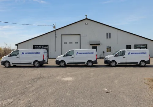 Three white vans with blue domain lettering lined up in front of the end wall of the light-gray storage hall with a roller door. In 2025, a total of 1,105 departures from Ülemiste were made for the evening rounds of Harju County.