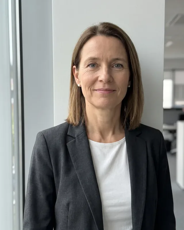 Margit Pärnaste in a dark gray jacket and white blouse is standing next to the big window of the office, the price quote shows the cleaning time for each room in minutes.