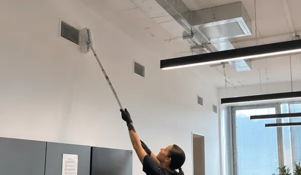 The cleaner cleans the air hole at the top of the wall with a brush with an extension handle, the dusty ventilation grate reduces the air exchange in the room.