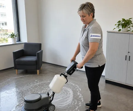 A cleaner operates a floor machine in an office with an armchair and a cabinet, a single-disc floor machine was purchased in 2012 for stone floors in downtown lobbies.