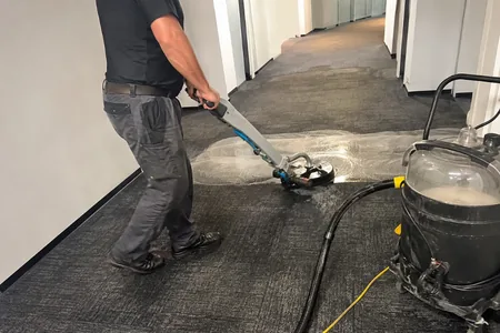 The operator cleans the office corridor carpet with an extraction device, an alcohol-based solvent is used to remove ink stains from office carpets.