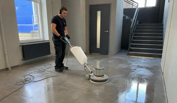 Kõrvaklappidega operaator poleerib ühekettalise põrandamasinaga trepihalli läikivat halli põrandat, poleeritud kivile ei kanta vaha, sest vaha muudab pinna kollakaks.