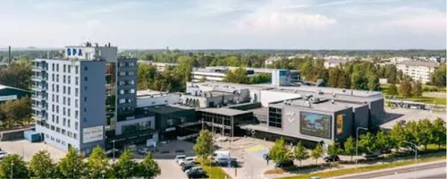 Ülaltvaade hõbedase fassaadiga kõrghoonele ja selle kõrval suure välisekraaniga kaubanduskeskusele, ees puudega ääristatud parkla, Viimsi kliinikute ooteruumi mänguasjad pestakse kord nädalas desinfitseeriva lahusega.